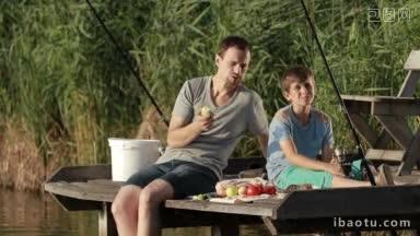 积极时尚的爸爸和十几岁的男孩在<strong>夏天</strong>的<strong>阳光下</strong>在木制浮筒上野餐，同时在湖边钓鱼